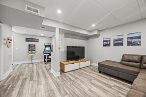 Ein modernes Wohnzimmer mit Flachbildfernseher, Spielkonsolen und einer Couch.