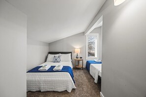 Ein Schlafzimmer mit zwei Betten, einem Nachttisch, einer Lampe und einem Fenster.