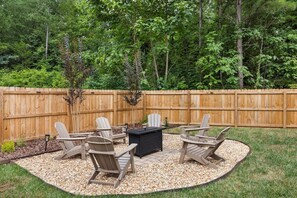En baghave med træterrasse, et cirkulært siddeområde med Adirondack-stole og en integreret pejseplads.