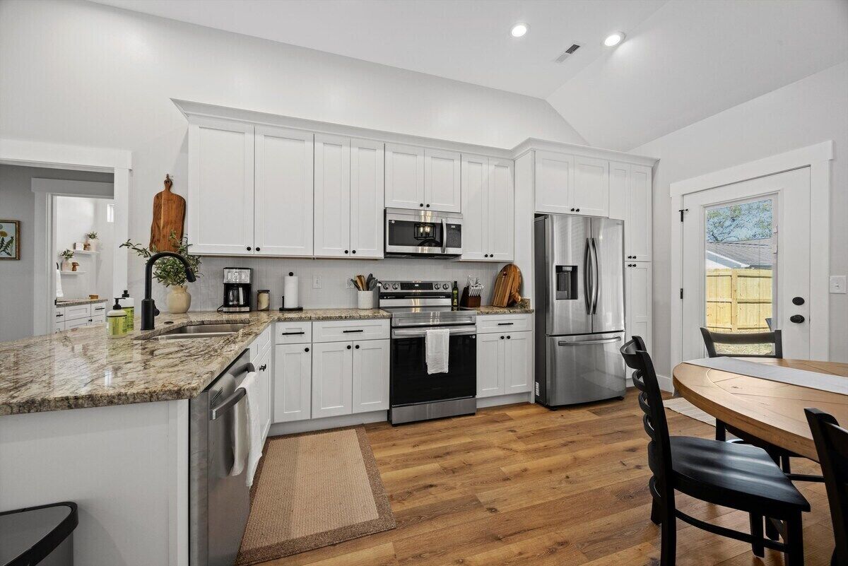 Una cocina moderna con armarios blancos, electrodomésticos de acero inoxidable y una mesa de comedor de madera.