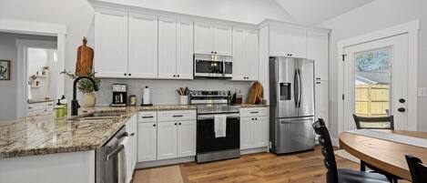 Una cocina moderna con armarios blancos, electrodomésticos de acero inoxidable y una mesa de comedor de madera.