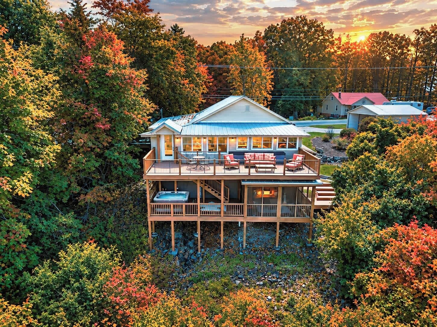 A two-story house with a deck, surrounded by trees and a sunset in the background.