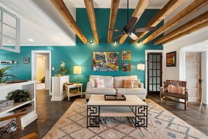A living room with a teal wall, wooden ceiling beams, a sofa, a coffee table, and a patterned rug. - Peach Bluff Retreat | Hot Tub | Gorgeous Views (Lookout Mountain)