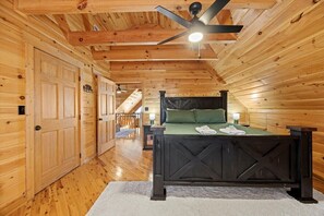 A wooden interior with a bed, a ceiling fan, and a hallway leading to another room. - Crossbow Cabin | Lookout Mountain • Stunning Views (Rising Fawn)