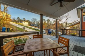 A covered outdoor deck with a table and chairs, overlooking a residential area with houses and a road. - Stellar View | North Shore Retreat | 30+ Nights (Chattanooga)