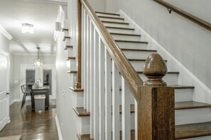 A staircase with wooden balusters and a white handrail, leading to a dining area with a table and chairs. - Stellar View | North Shore Retreat | 30+ Nights (Chattanooga)