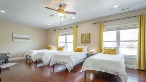 Ein Hotelzimmer mit drei Betten, einem Deckenventilator und großen Fenstern mit Vorhängen.