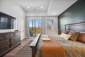 A bedroom with a large bed, a dresser, a bench, and a television on the wall. - Hunters Ridge | Rustic Modern • Hot Tub • Goats! (Rossville)