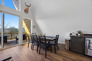 Ein Essbereich mit Tisch und Stühlen, eine Küche mit Spüle und Schränken sowie ein großes Fenster mit Blick auf eine Terrasse.