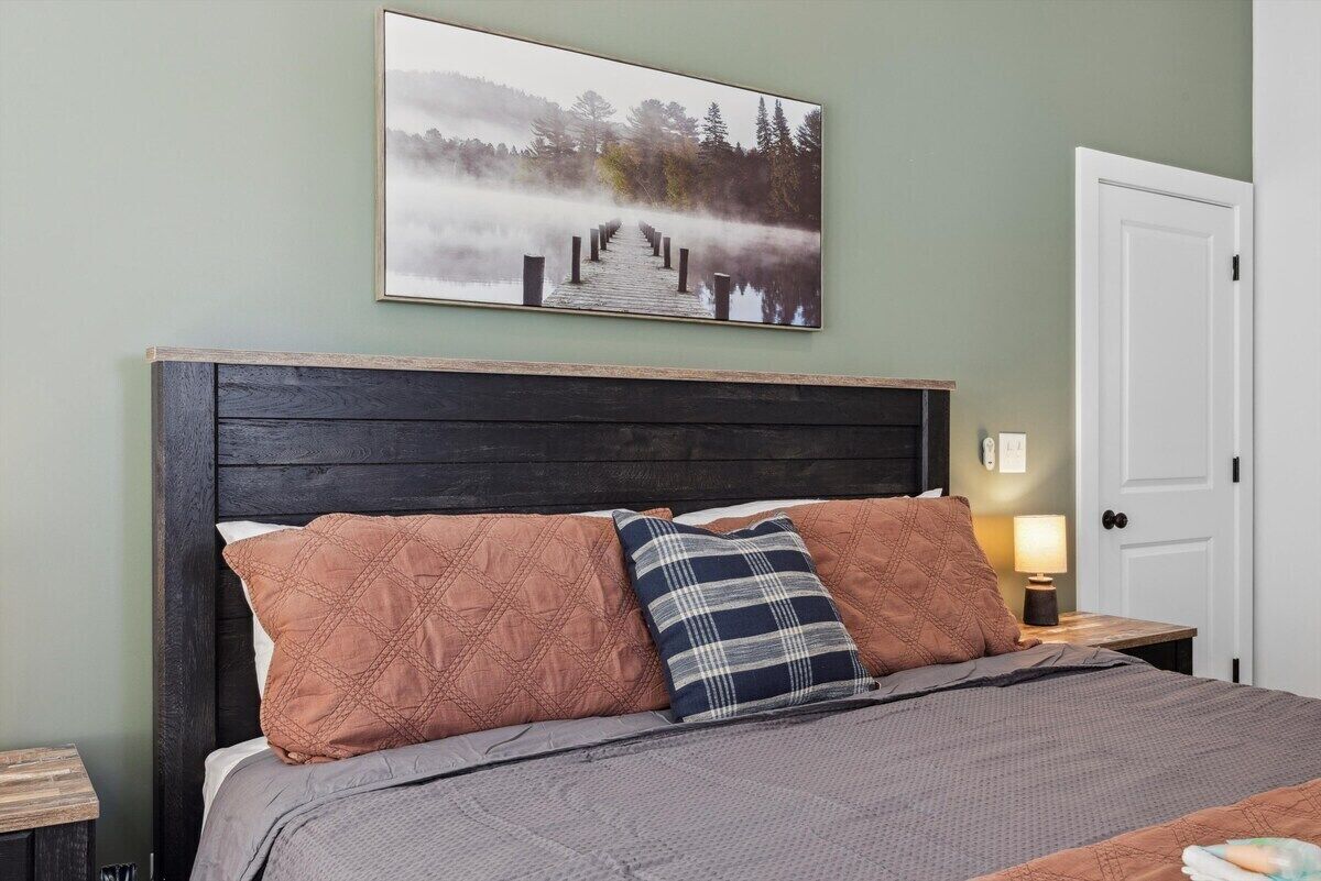 Una camera da letto con una testiera in legno, un letto con biancheria a motivi, un comodino con una lampada e un quadro con una banchina avvolta nella nebbia.