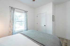 A bedroom with a bed, a window with curtains, a door, and a framed picture on the wall. - Cloudland Summit | Hot Tub + Grill | Dog Friendly (Rising Fawn)