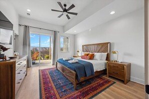 Une chambre à coucher comprenant un lit, une table de chevet, un bureau, un ventilateur de plafond et une vue sur l’extérieur.