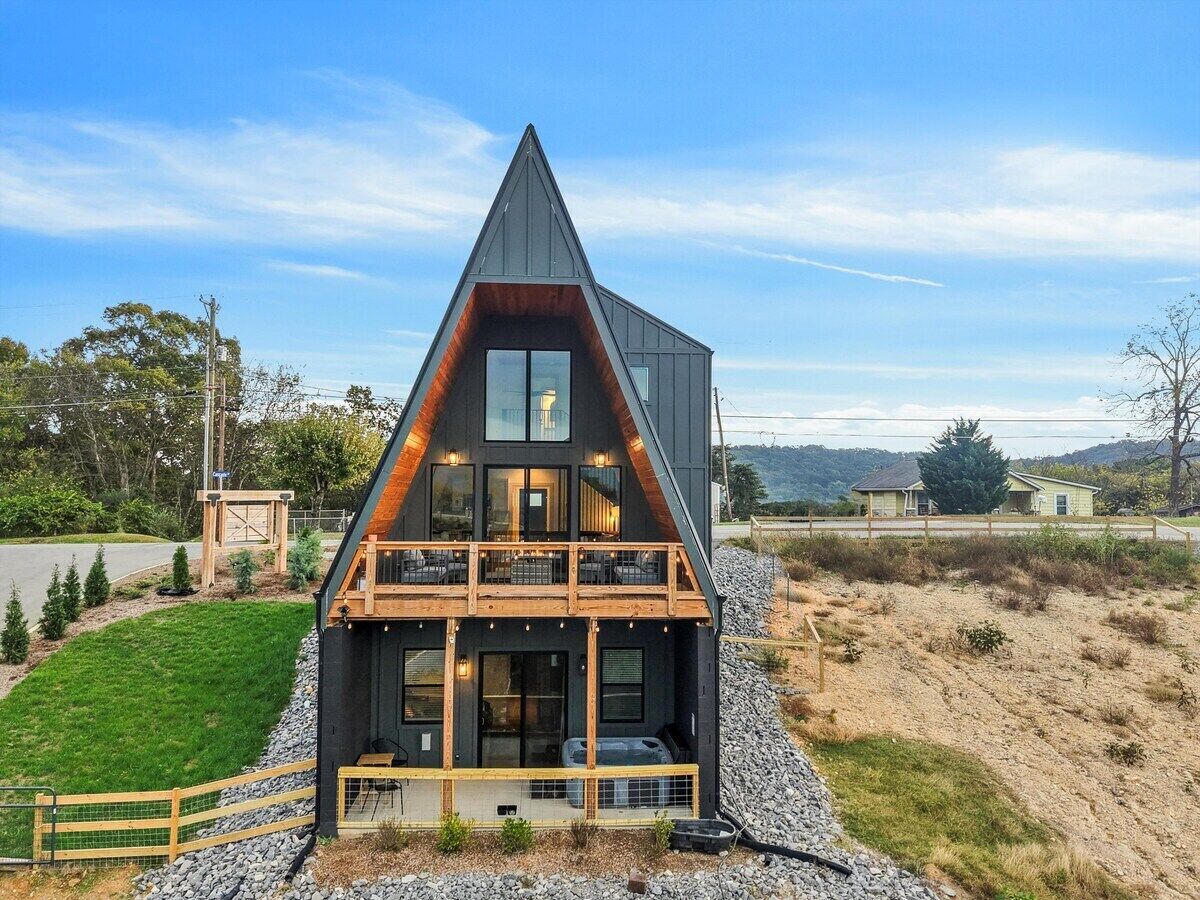 A modern two-story house with a prominent triangular roof, a balcony on the upper floor, and a well-maintained lawn.