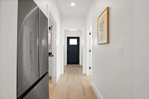 A hallway with a modern kitchen area on one side, a black door at the end, and a framed picture on the wall. - Alpine A-Frames | 6 Luxe Cabins | Sleeps 60! (Rossville)