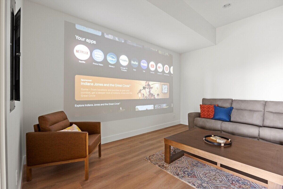 Un soggiorno moderno con un grande schermo che mostra una selezione di app di streaming, un divano in pelle marrone, un tavolino in legno e un tappeto decorato.