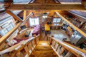 Ein Holzhaus-Interieur mit einer Holzwindeltreppe, einer Küchenzeile und einem Wohnbereich mit Sofa und Esstisch.