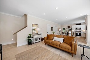 A modern living room with a brown leather sofa, a coffee table, and a staircase leading to another level. - Bluebird Cottage | Near Downtown | Walking Trails! (Chattanooga)