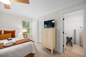A bedroom with a bed, a television on a cabinet, a window with a view of trees, and a door leading to another room. - Bluebird Cottage | Near Downtown | Walking Trails! (Chattanooga)