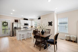 Une cuisine moderne dotée d’un îlot central, de meubles blancs et d’un coin repas avec une table et des chaises en bois.