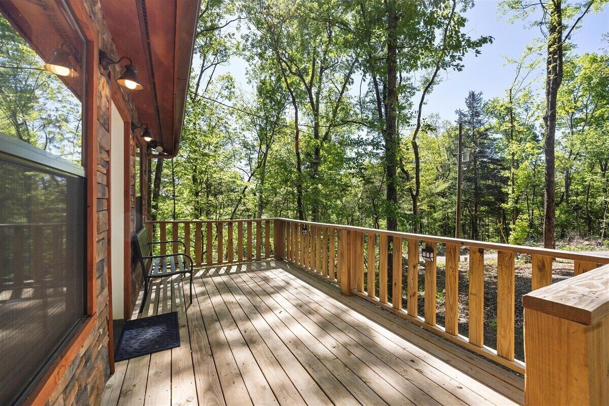 A wooden deck with a railing, a bench, and a door leading to a screened area.