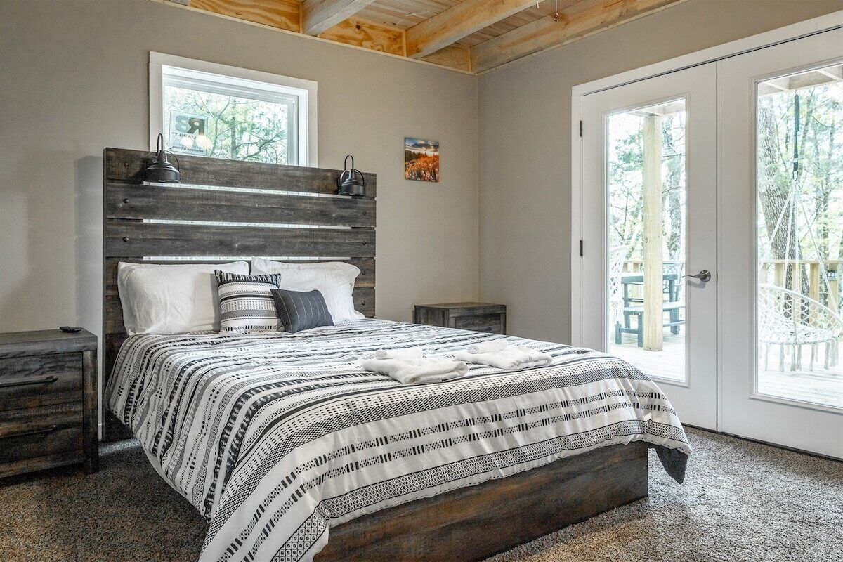 A bedroom with a bed, a nightstand, a wooden headboard, a window, and a door.