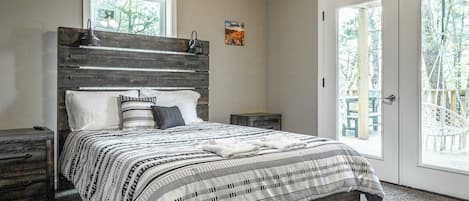 Un dormitorio con una cama, una mesita de noche, un cabecero de madera, una ventana y una puerta.