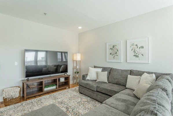 A modern living room with a flat-screen TV, grey sofa, and two framed botanical prints on the wall. - The Southie | Minutes from Downtown Chatt! (Chattanooga)