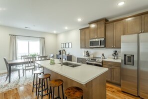 A modern kitchen with wooden cabinets, stainless steel appliances, and a central island with stools. - The Southie | Minutes from Downtown Chatt! (Chattanooga)