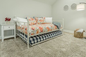 A bedroom with a white metal bed frame, floral bedding, a small bedside table with a drawer, a bedside lamp, and a decorative wall with two circular patterns. - The Southie | Minutes from Downtown Chatt! (Chattanooga)