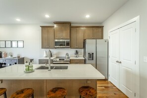 A modern kitchen with wooden cabinets, stainless steel appliances, and a large island with stools. - The Southie | Minutes from Downtown Chatt! (Chattanooga)