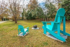 A turquoise Adirondack chair and a fire pit in a grassy outdoor area with trees. - Lake Hills Landing | Family Friendly+Hot Tub+EV (Trenton)