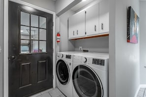 A laundry room with a dark door, two front-loading washing machines, white cabinets, and a fire extinguisher on the wall. - Lake Hills Landing | Family Friendly+Hot Tub+EV (Trenton)