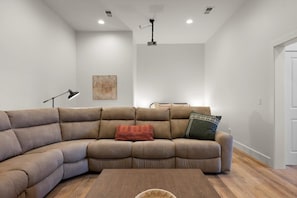 Ein modernes Wohnzimmer mit einer Eckcouch, einem Couchtisch und einem Deckenprojektor.