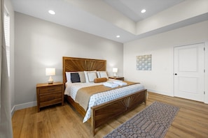 Ein Schlafzimmer mit einem hölzernen Bett, Nachttischen, einem Beistelltisch, einem gemusterten Teppich und einer weißen Tür.