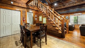 A wooden interior with a staircase, dining table, chairs, and a fire extinguisher. - Hideaway Lodge | Rustic W/ Hot Tub! Pet Friendly (Trenton)