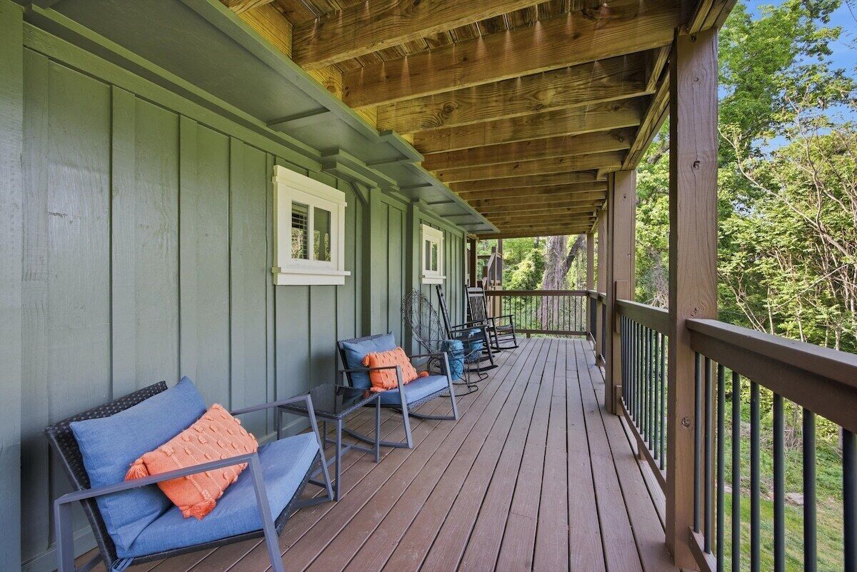A covered porch with wooden railings and a series of chairs with cushions.