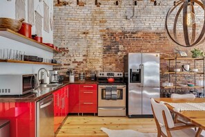 A kitchen with red cabinets, a stainless steel refrigerator, and a brick wall. - Saint Elmo Loft | Upscale Retreat • Near Downtown! (Chattanooga)