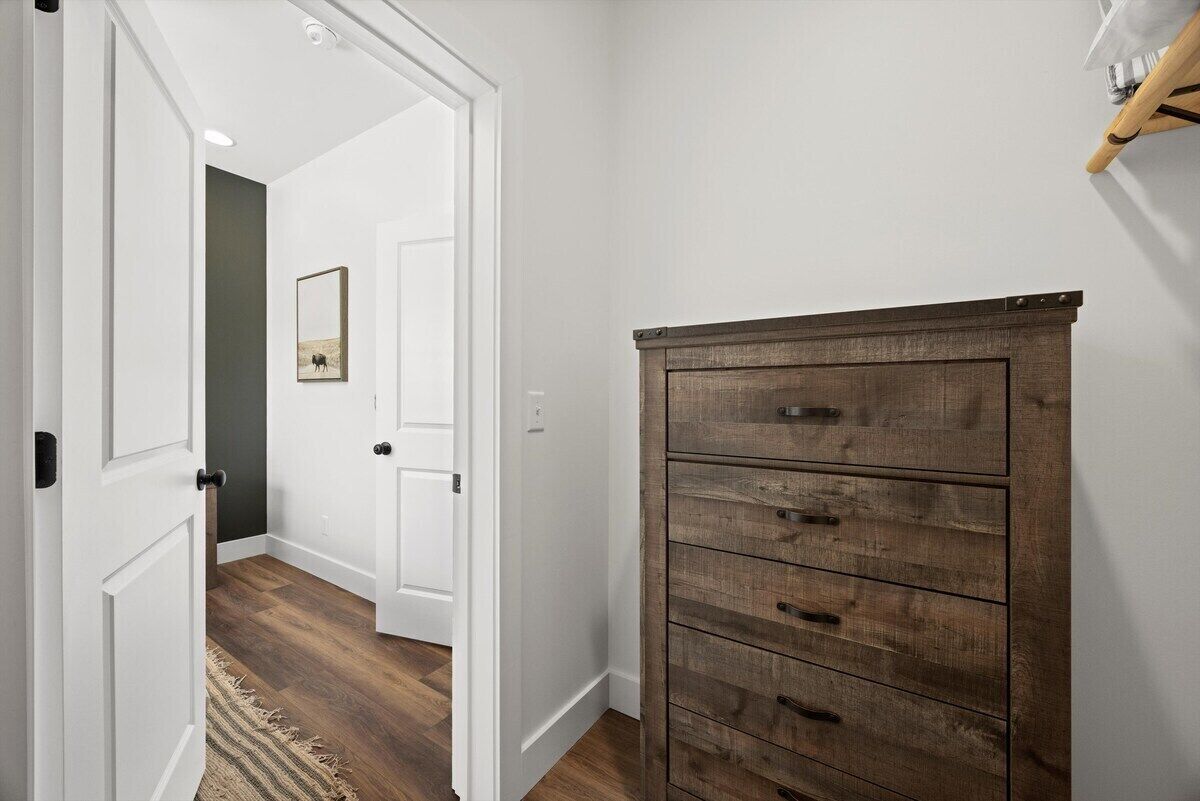 A hallway with a wooden dresser, white walls, and a door leading to another room.