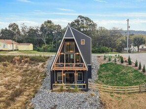 A modern two-story house with a prominent gable roof, large windows, and a balcony. - Buffalo Bluff | A-Frame Retreat | Pet Baby Goats! (Rossville)