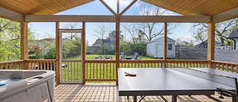 A covered outdoor area with a hot tub, ping pong table, and a view of a backyard.