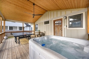 Un bain à remous sur une terrasse en bois, avec un ventilateur de plafond, une table avec des chaises et une porte avec une fenêtre.
