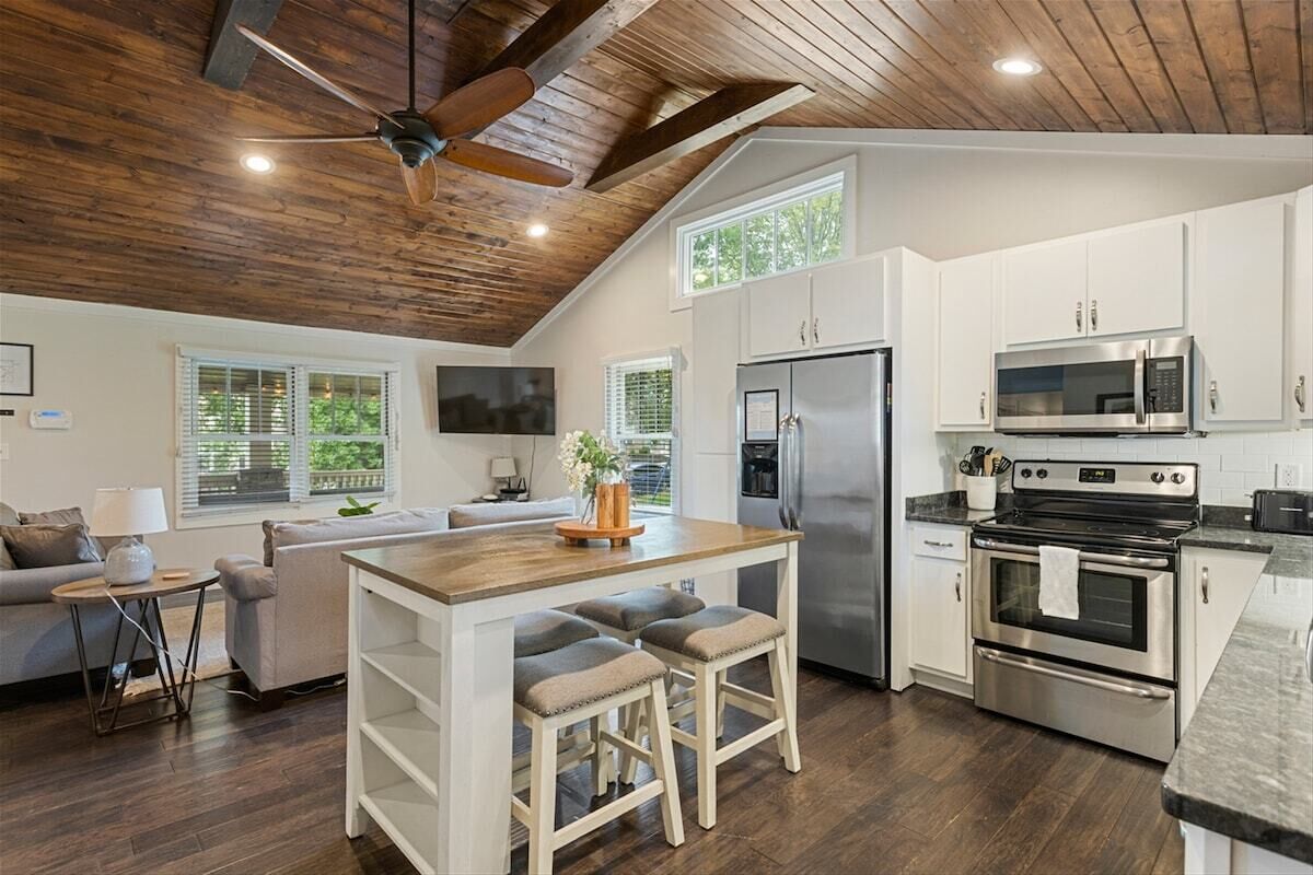 A modern kitchen with white cabinets, stainless steel appliances, and a wooden ceiling.