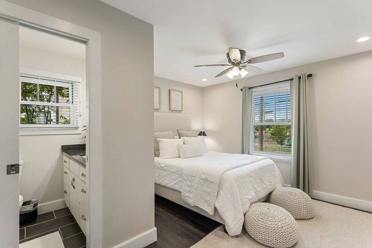 A bedroom with a bed, a ceiling fan, a window with curtains, and a view of trees outside.
