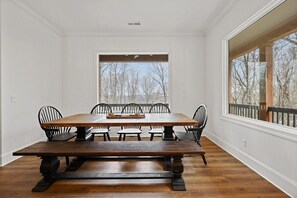 A dining room with a large wooden table and six chairs, a window with a view of trees, and a balcony with a railing. - Emerald Lodge | Epic Mtn Cabin | Hot Tub + Views (South Pittsburg)