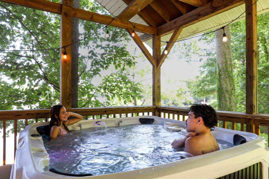 Un bain à remous où se trouvent deux personnes, entouré d’une terrasse en bois et d’arbres.