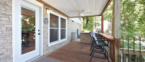 Un patio cubierto con terraza de madera, una zona de estar con sillas y vistas a la vegetación circundante.