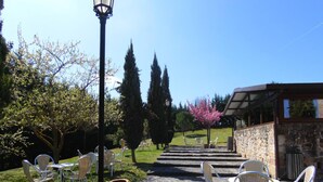 Un espace extérieur aménagé avec des sièges, accessible par des marches en pierre menant à un patio couvert, le tout entouré de verdure et d’arbres.
