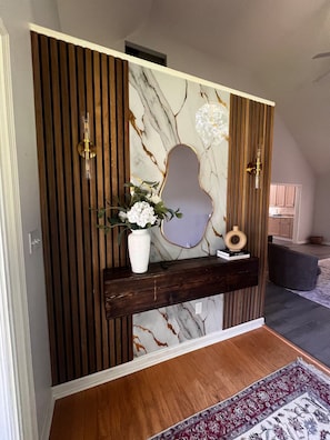 Una consola de madera con panel trasero de mármol, un florero con flores y un espejo decorativo.