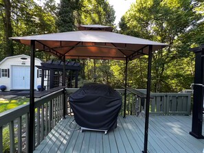 Um deck coberto ao ar livre com churrasqueira, pérgola e uma garagem branca.