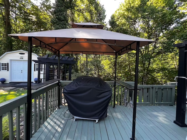 Una terraza cubierta al aire libre con una parrilla, un pérgola y un garaje blanco.